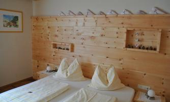 A cozy bedroom with a wooden design. There are two beds with pillows and decorative elements on the wall.