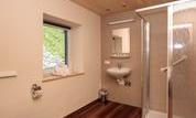 A modern bathroom with a shower, a sink, and a toilet. The floor is made of wood and there is a window with a view.