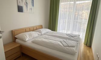 A cozy bedroom with a double bed and two nightstands. Large windows provide plenty of natural light and a view outside.