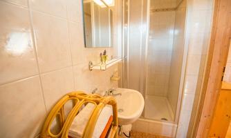 A modern bathroom with a shower cubicle and a sink. Towels are nicely arranged on a rattan shelf.