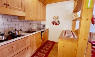 A cozy kitchen with wooden cabinets and modern appliances. A red runner lies on the floor, giving the room a warm atmosphere.