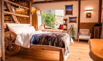 A cozy bedroom with a rustic wooden bed and a unique wheel design. Lush greenery can be seen through the window, creating a pleasant atmosphere.