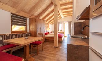 A cozy, modern room with wooden furnishings and a double bed. The dining area is equipped with a wooden dining table and red chairs.