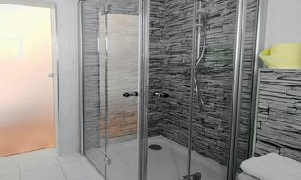 A modern shower with glass walls and an elegant stone wall covering. The floor is bright and spacious, and fresh towels are stacked nearby.