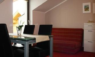A cozy room with a dining area, a sofa, and a colorful carpet. The light falls through the window, creating an inviting atmosphere.