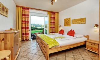 A cozy hotel room with a double bed and red pillows. Large windows offer a view of the green landscape.