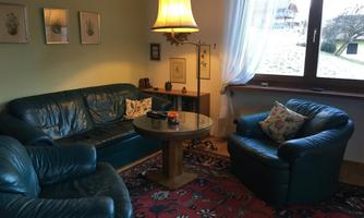 A cozy living room with a green leather couch and a round table. The light from the floor lamp creates an inviting atmosphere.