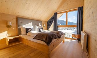 A cozy bedroom with wooden paneling and a large window that offers a view of the mountains. The bed is inviting and the decor is modern and simple.