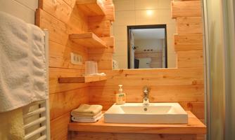 A modern bathroom with wooden paneling and a sink. In the background, towels and a mirror are visible.