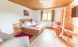 A cozy bedroom with wooden furniture and a large bed. The room has a warm wooden floor and large windows with curtains.
