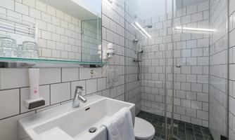 A modern bathroom with white tiles and a glass shower. The sink is simple and elegant, with towels and toiletries.