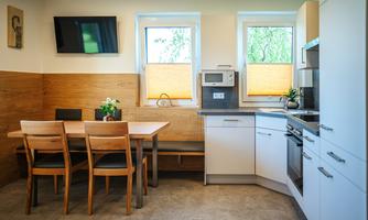 A modern kitchen with wood paneling and a small dining area. It is bright and well-equipped.