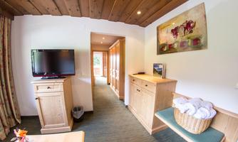 A cozy hotel room with wooden furniture and a flat-screen TV. The space is bright and inviting, with a door leading to a hallway.