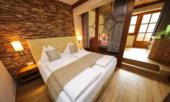 A modern bedroom with a large bed and wooden accents. Large windows provide plenty of daylight.