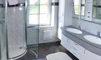 A modern bathroom with a shower cubicle and two sinks. The walls are brightly tiled and there is a large window for natural light.