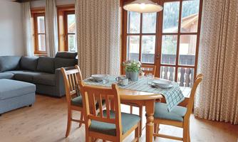A cozy dining area with a round table and four chairs. Large windows let in plenty of light and offer a view of nature.