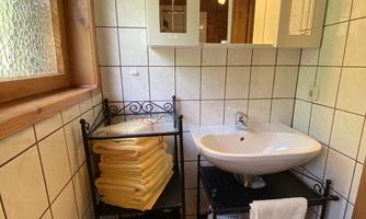 A cozy bathroom with a modern sink and a large mirror. Towels are neatly stacked on a shelf.