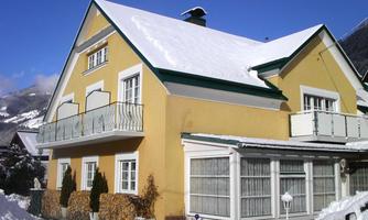 A yellow house with a green roof and a balcony. The snow is visible around the house.