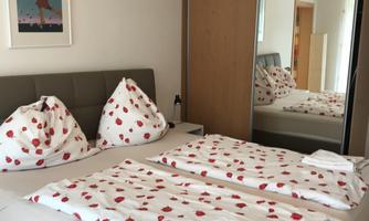 A cozy bedroom with a double bed and attractive floral patterned bedding. In the background, the room is reflected in the large wardrobe.
