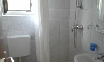 A small bathroom with a shower, sink, and toilet. Bright, tiled walls and a window provide light.