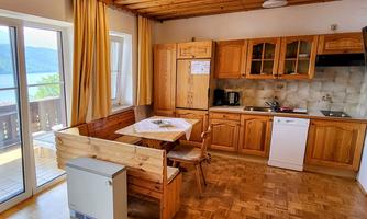 A bright kitchen with wooden furniture and a dining table. Through the window, there is a beautiful view of the lake.
