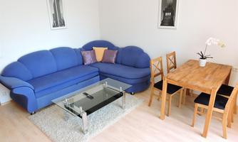 A cozy living room with a blue sofa and a wooden table. The room is bright and furnished in a modern style.