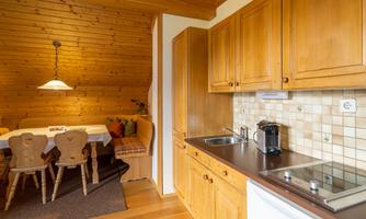 A cozy kitchen with wooden cabinets and modern appliances. Next door is a dining area with a table and chairs.
