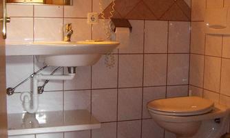 A simple bathroom with a sink and a toilet. The walls are adorned with white tiles and a decorative pattern.