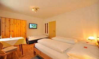 A cozy room with two beds and a television. There is a table with chairs and a wooden wardrobe.
