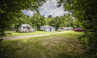 A beautiful campsite with several caravans and a holiday home, surrounded by trees. The sky is slightly cloudy and the area is green and well-maintained.
