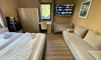 A cozy room with a double bed and a sofa. A television hangs on the wall, and there is a desk as well as a wardrobe.