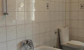 A modern bathroom with a bathtub and a toilet. The walls are designed with white tiles and decorative accents.