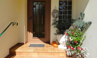 Inviting entrance area with a brown door and flower arrangements. The steps are made of light tiles, and next to the door are pots with plants.