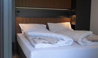 A modern bedroom with two separate beds and wooden panels on the wall. The bedding is neatly folded and the light is soft.