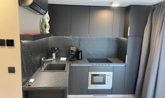 A modern, well-equipped kitchenette with gray cabinets and a marble wallpaper. The kitchen includes a stove, an oven, and a coffee machine.