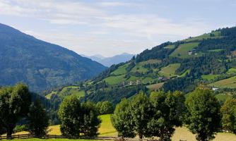 A picturesque landscape with gentle hills and green meadows. In the background, mountains and a clear sky can be seen.