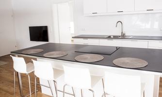 A modern kitchen with a large kitchen island, chairs, and a sink. The furniture is in light colors, creating an inviting atmosphere.
