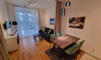 A modern living room with a dining table and chairs. Large windows provide plenty of daylight.