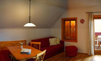 A cozy living room with a red sofa and a wood-colored dining table. Large windows let in plenty of light and provide access to an outdoor terrace.