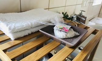 A wooden tray with a small gift on a bathroom shelf. In the background, fresh, white towels are laid out.