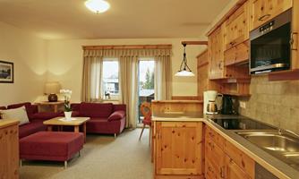 A cozy living space with red sofas and a wooden cabinet. The open kitchen is modern and well-equipped.
