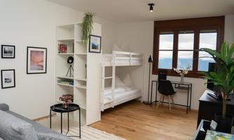 A modern room with a bunk bed and a desk.  
Bright walls and large windows create a pleasant atmosphere.