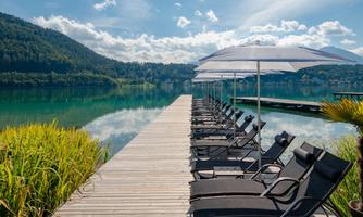 A quiet dock by the lake with loungers and sun umbrellas. Surrounded by green hills and clear water.