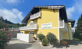 A yellow house with balconies and a garden. It is a holiday property with flowering plants in the foreground.