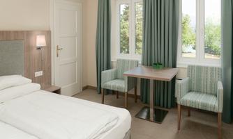 A modern hotel room with two single beds and bright colors. There is a small table with two chairs and large windows that let in a lot of daylight.