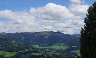 An impressive mountain landscape with green meadows and a cloudy sky. Steep hills stretch into the distance.