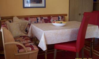 A cozy dining area with a table and red chairs. On the table, there is a bowl of fruit.