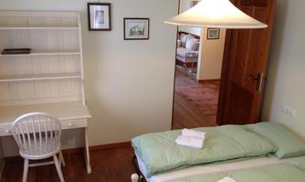 A cozy bedroom with two single beds and fresh linens. A desk and a lamp create a bright and friendly atmosphere.
