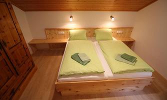 A cozy room with two single beds and fresh, light green bedding. The walls and furniture are made of light wood, creating an inviting atmosphere.