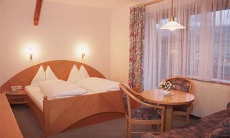 A cozy hotel room with a double bed and a small dining area. Large windows provide plenty of daylight and a pleasant atmosphere.